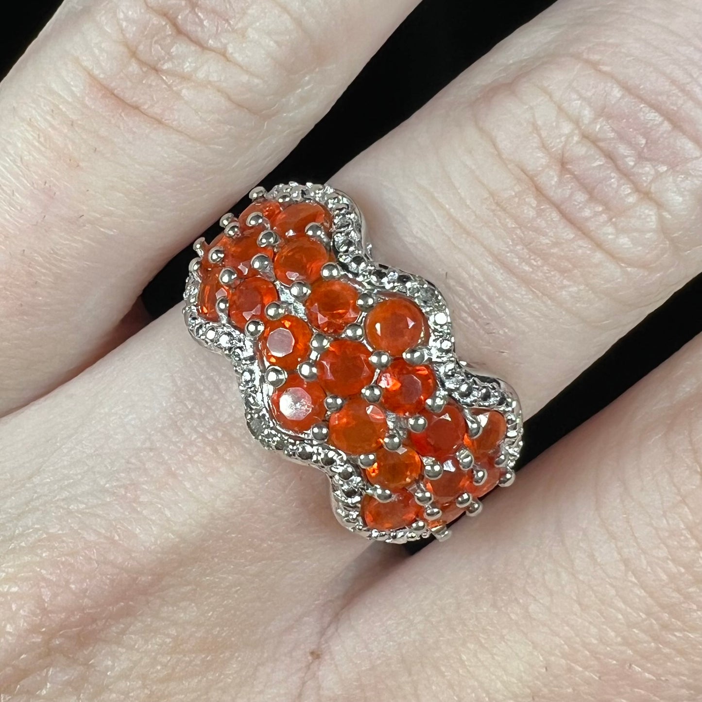 Close-up macro view of a sterling silver Mexican fire opal and diamond-accent ring, worn on a finger.