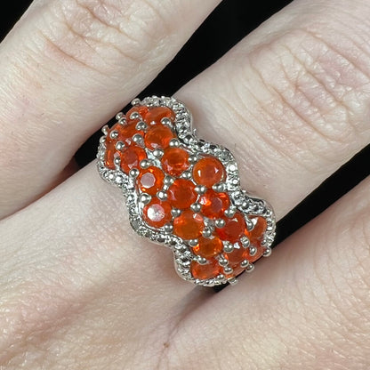 Close-up macro view of a sterling silver Mexican fire opal and diamond-accent ring, worn on a finger.