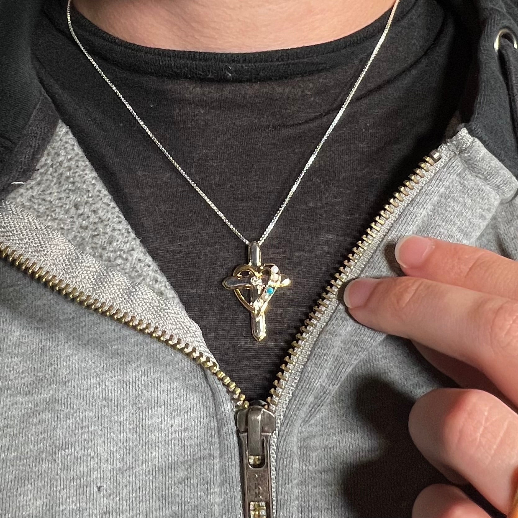 A sterling silver mother's cross necklace set with diamond, opal, turquoise, and pearl, worn around a neck.