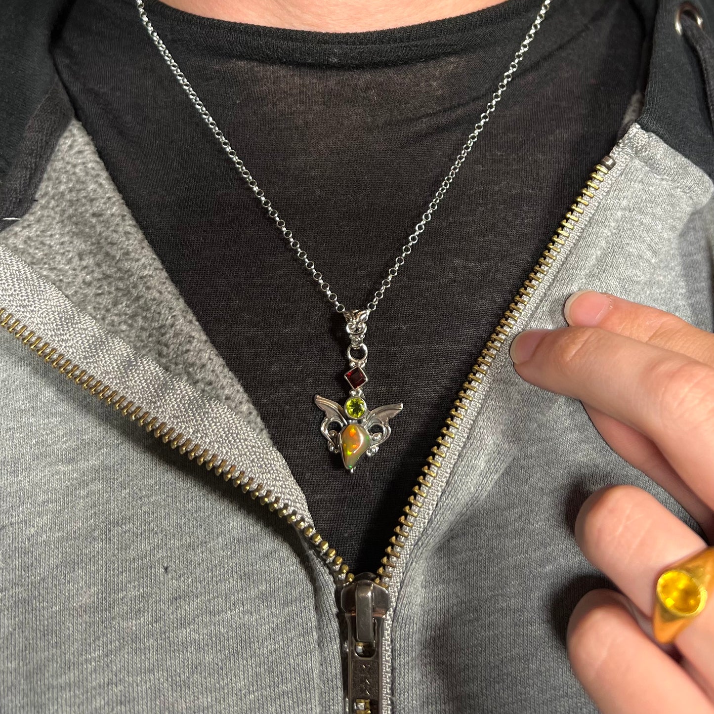 A sterling silver angel necklace set with an Ethiopian fire opal, peridot, and garnet, worn around a neck.