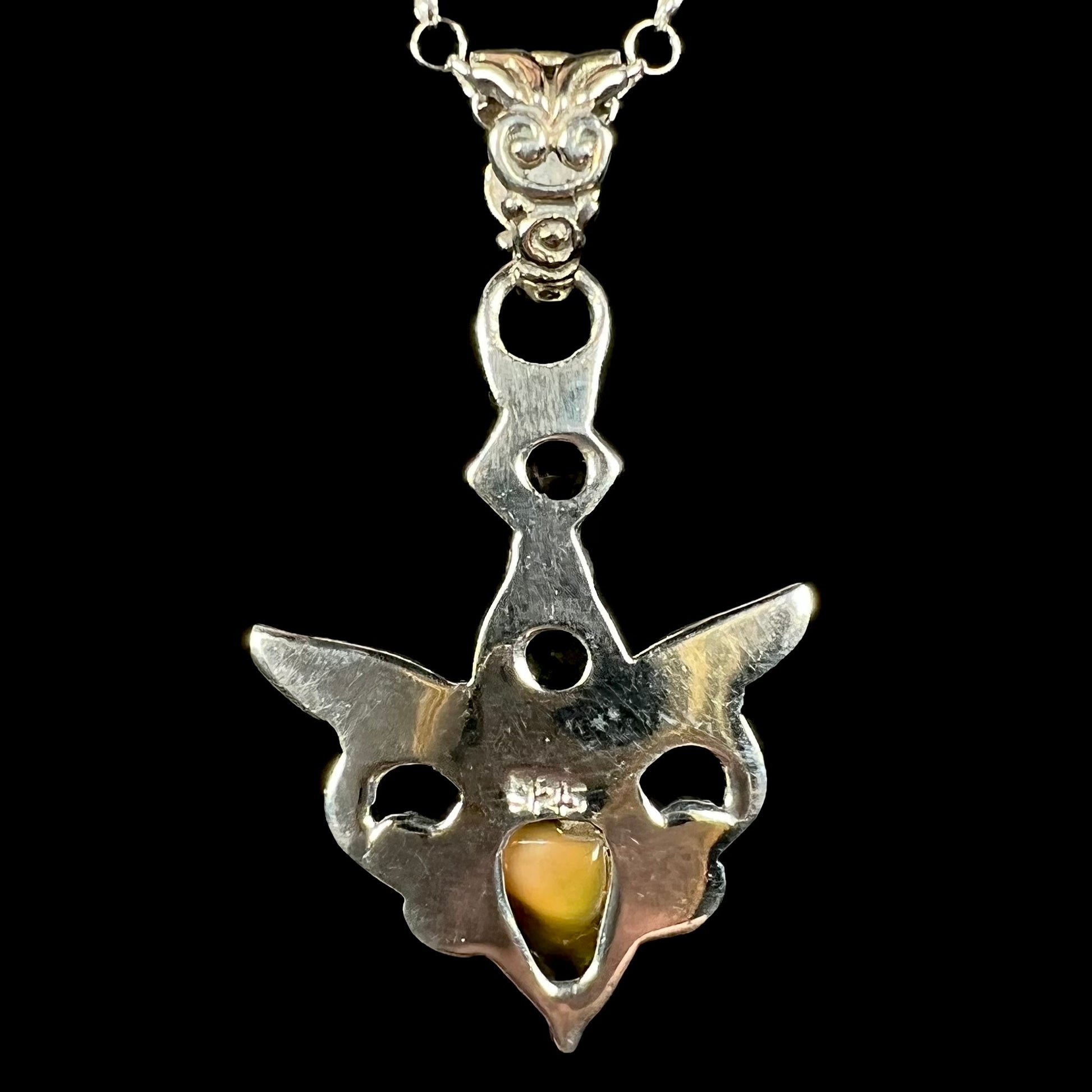Back side of a sterling silver Ethiopian opal angel pendant shown against a black background.