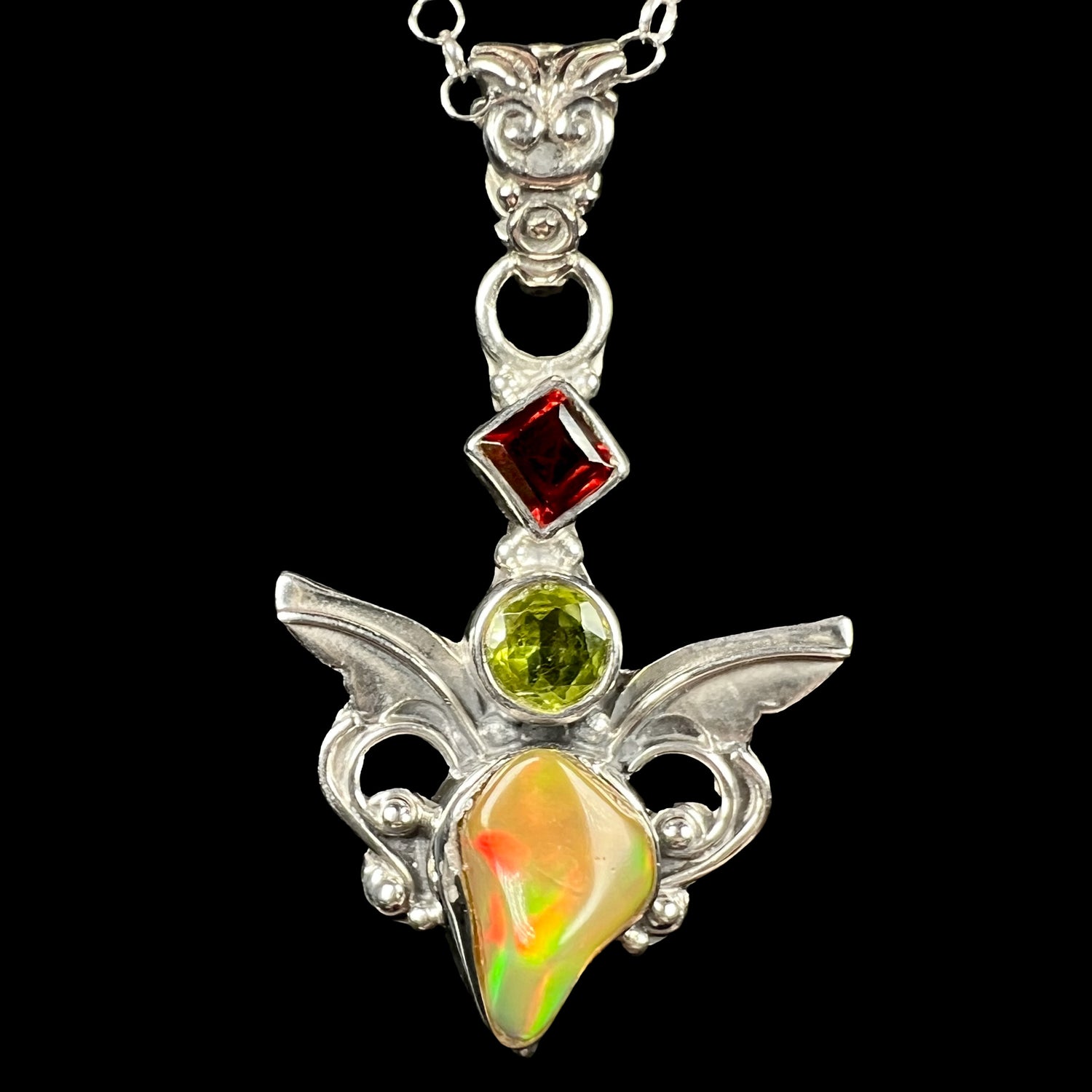 A sterling silver angel pendant set with an Ethiopian fire opal, peridot, and garnet, shown close-up from the front.