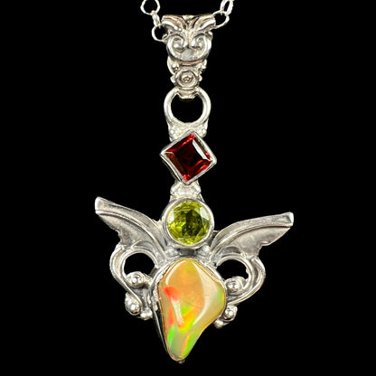 A sterling silver angel pendant set with an Ethiopian fire opal, peridot, and garnet, shown close-up from the front.
