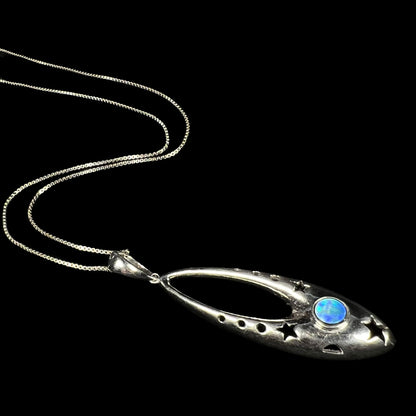 A sterling silver and opal doublet ballerina shoe necklace shown from an angle laying on a black background.