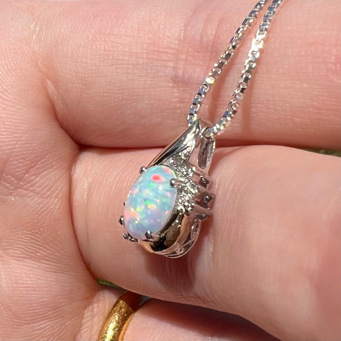 A sterling silver synthetic opal and diamond pendant by Alwand Vahan, shown close-up from an angle in sunlight.