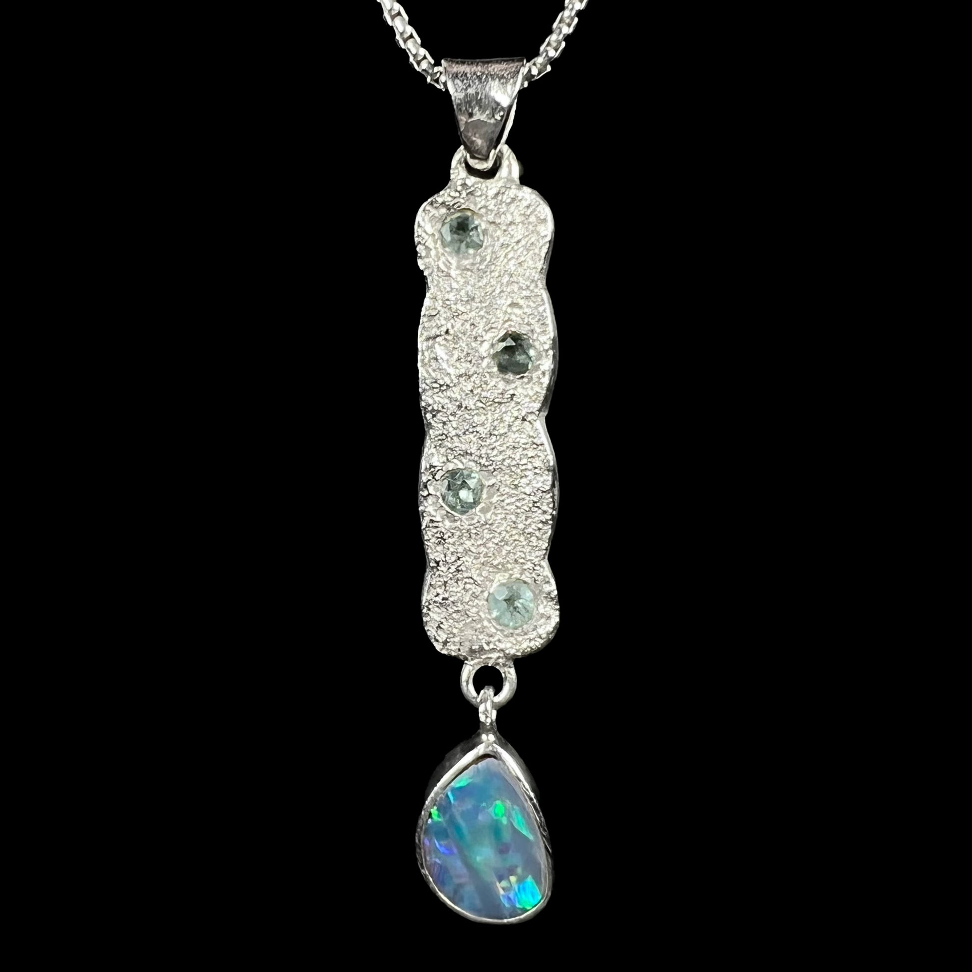 Close-up of an estate sterling silver opal doublet and blue topaz-accented drop pendant shown from the front side against black backdrop.