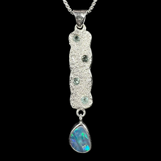 Close-up of an estate sterling silver opal doublet and blue topaz-accented drop pendant shown from the front side against black backdrop.