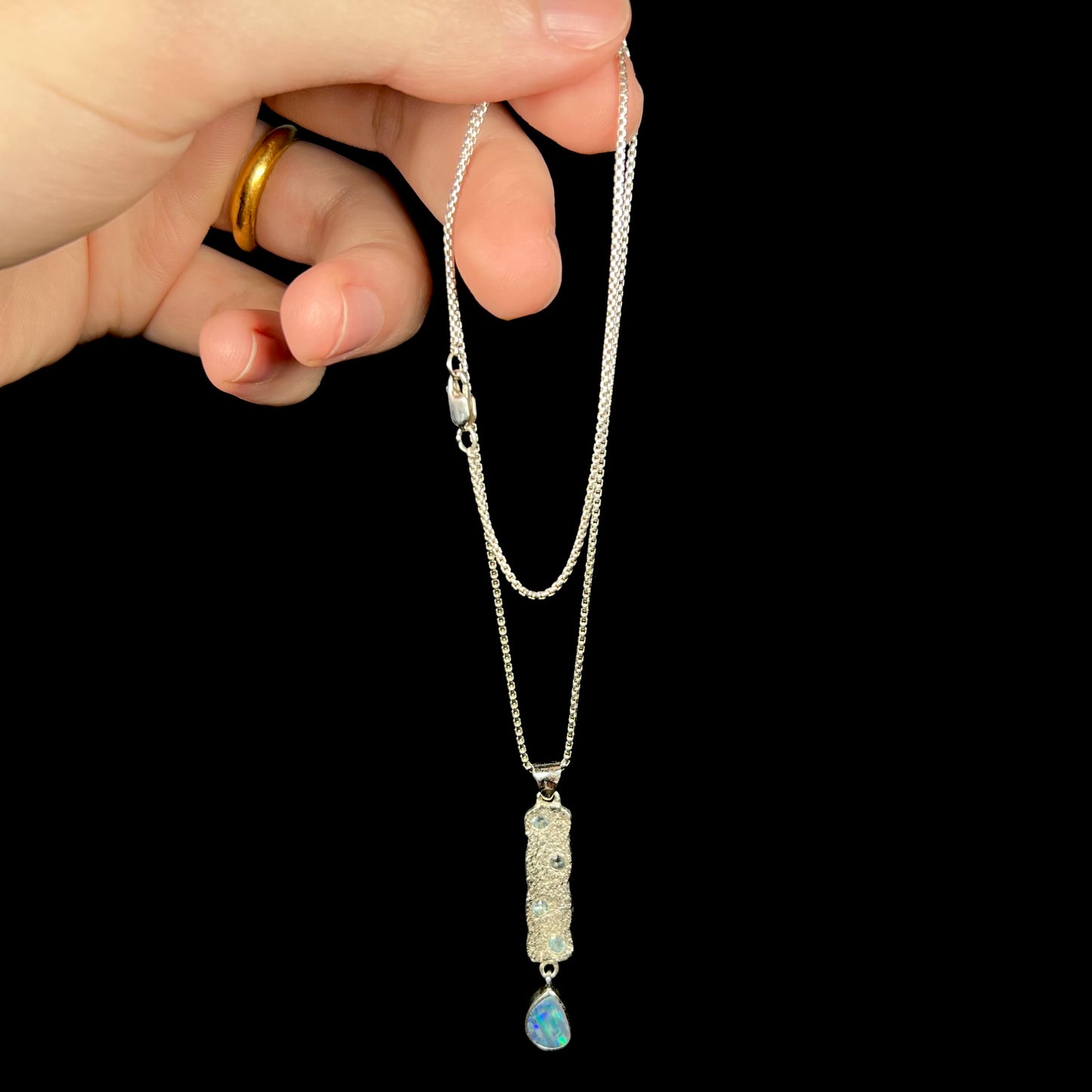 Hand dangling a sterling silver opal doublet and blue topaz-accented necklace from its rounded box-style chain.