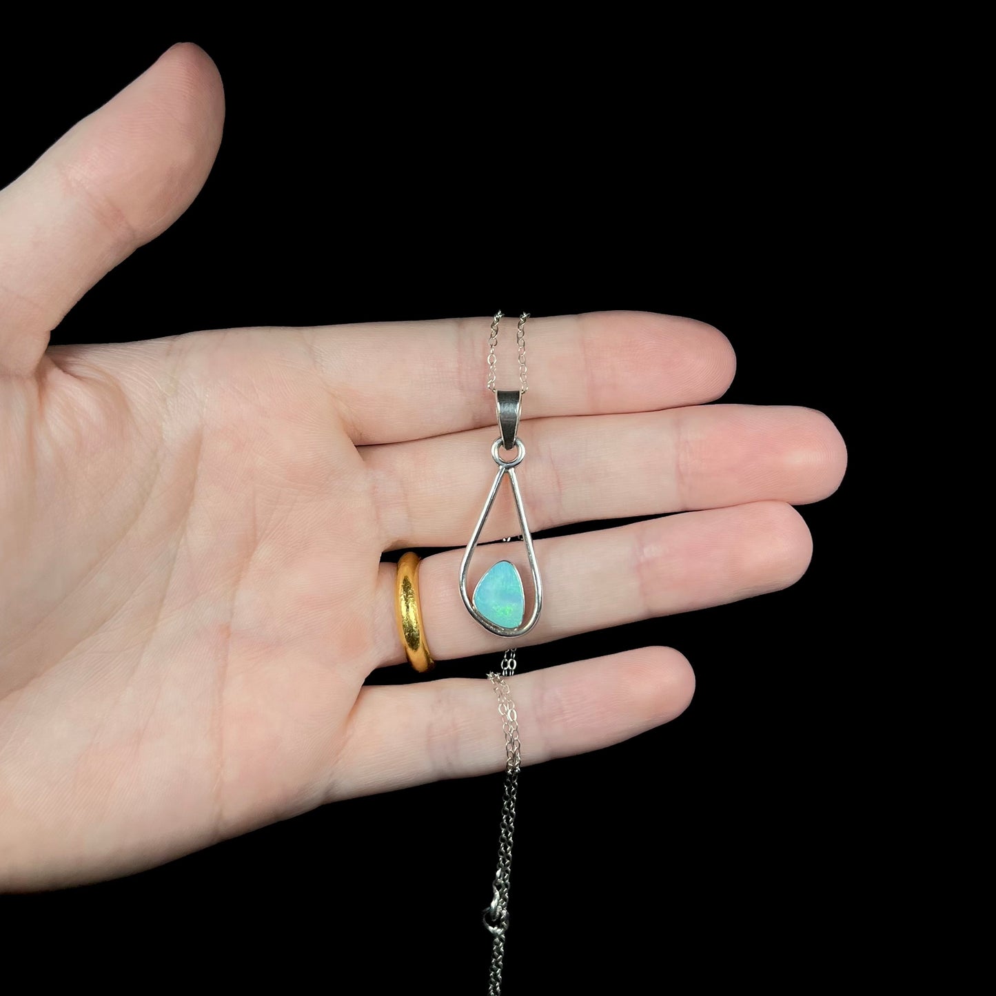 Hand holding a sterling silver necklace with a green opal doublet pendant against a black background.
