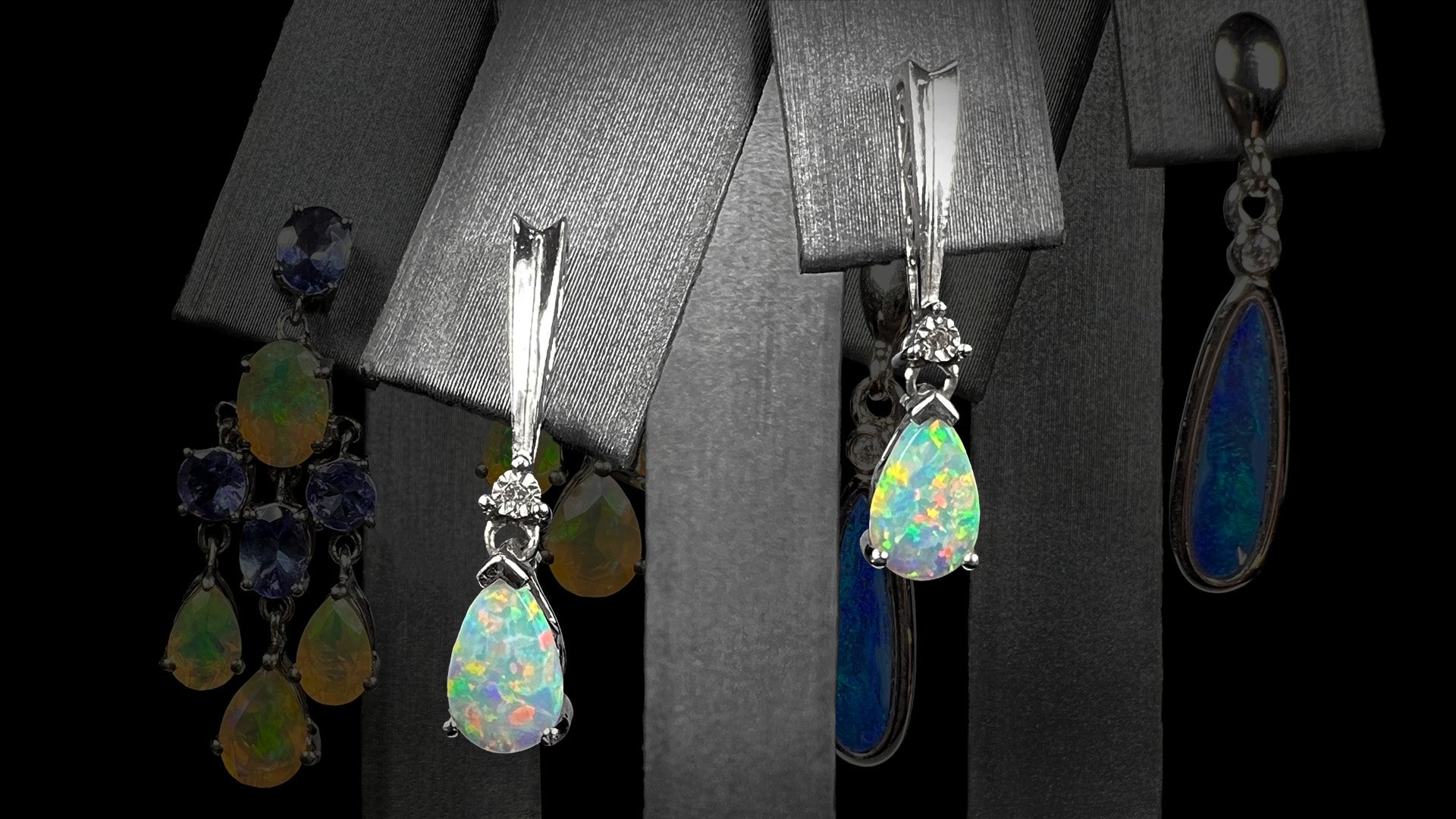 A pair of sterling silver lab-created opal dangle earrings shown on an earring display in front of two pairs of artistically faded sterling silver dangle earrings.