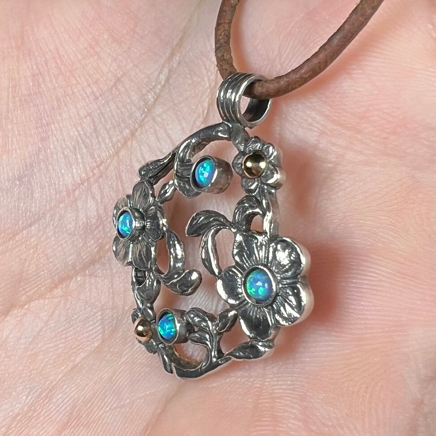A two-tone sterling silver and 14k gold opal dogwood flower pendant shown from an angle close-up in a hand.