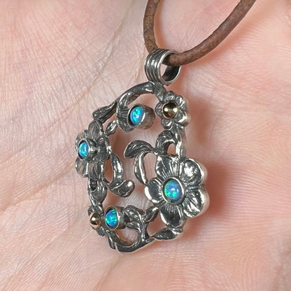 A two-tone sterling silver and 14k gold opal dogwood flower pendant shown from an angle close-up in a hand.