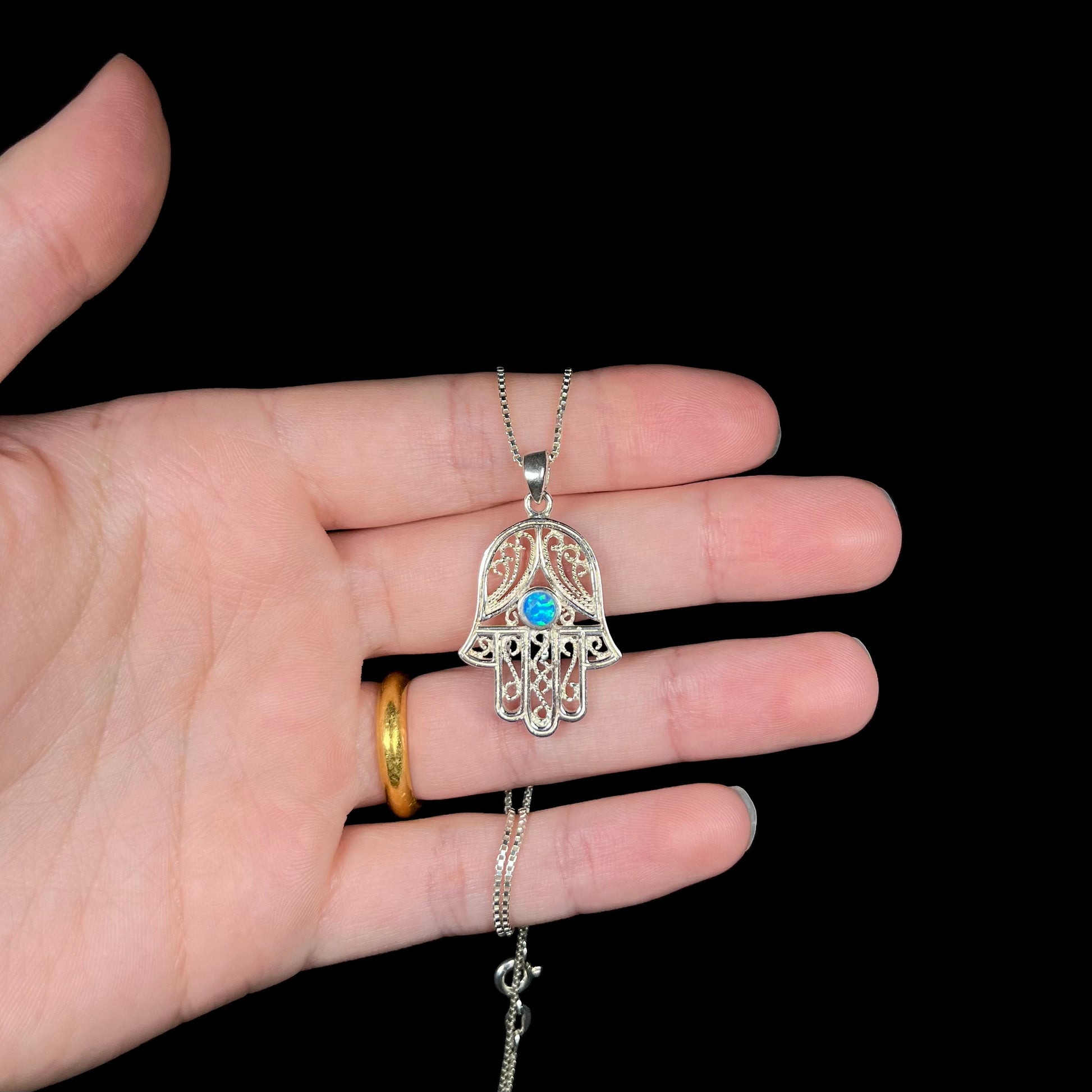 A sterling silver and filigree-accented hamsa hand necklace set with a round lab-created opal.