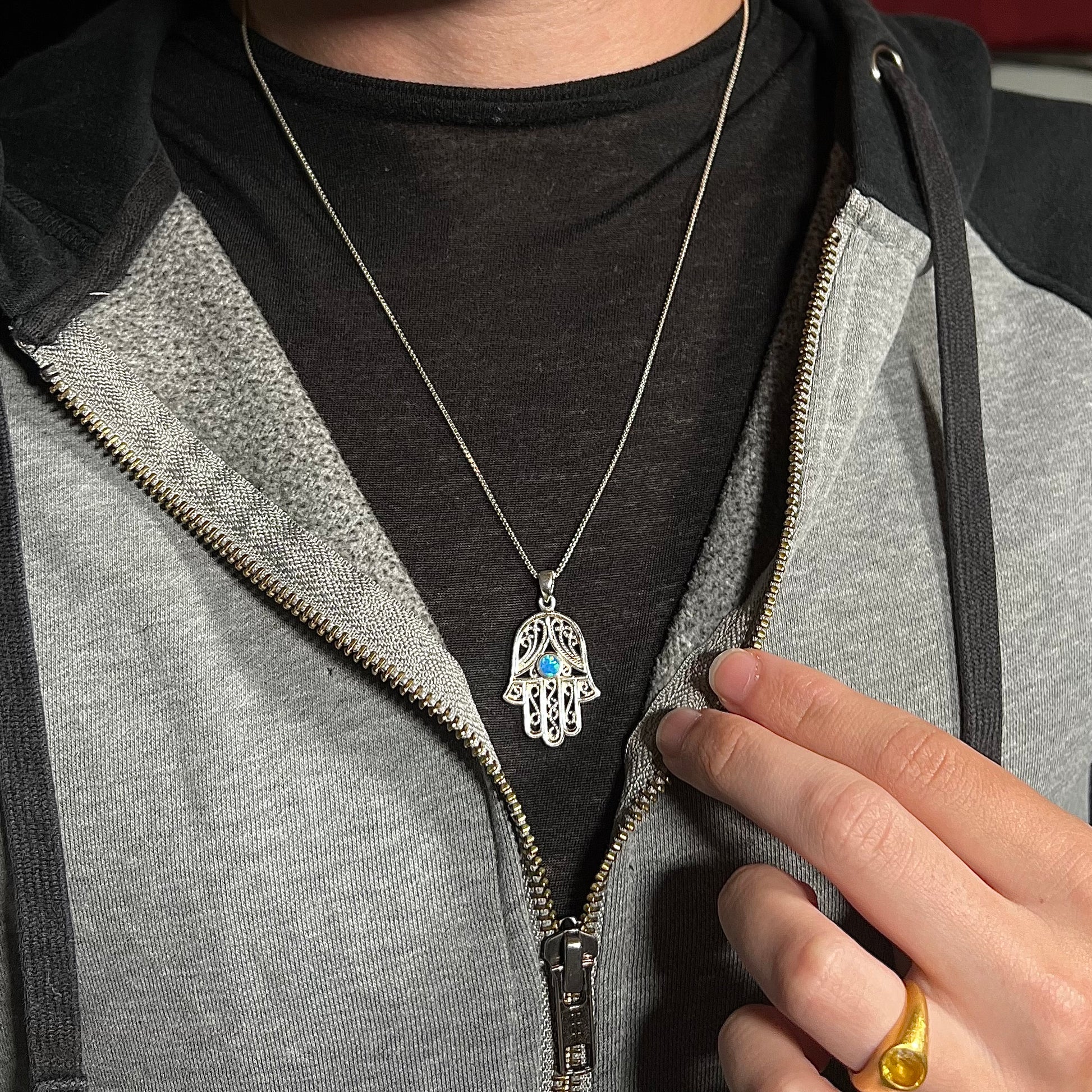 A sterling silver and filigree-accented hamsa hand necklace set with a round lab-created opal, worn around a neck.