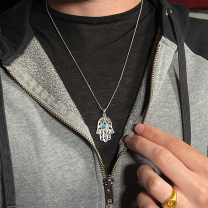A sterling silver and filigree-accented hamsa hand necklace set with a round lab-created opal, worn around a neck.