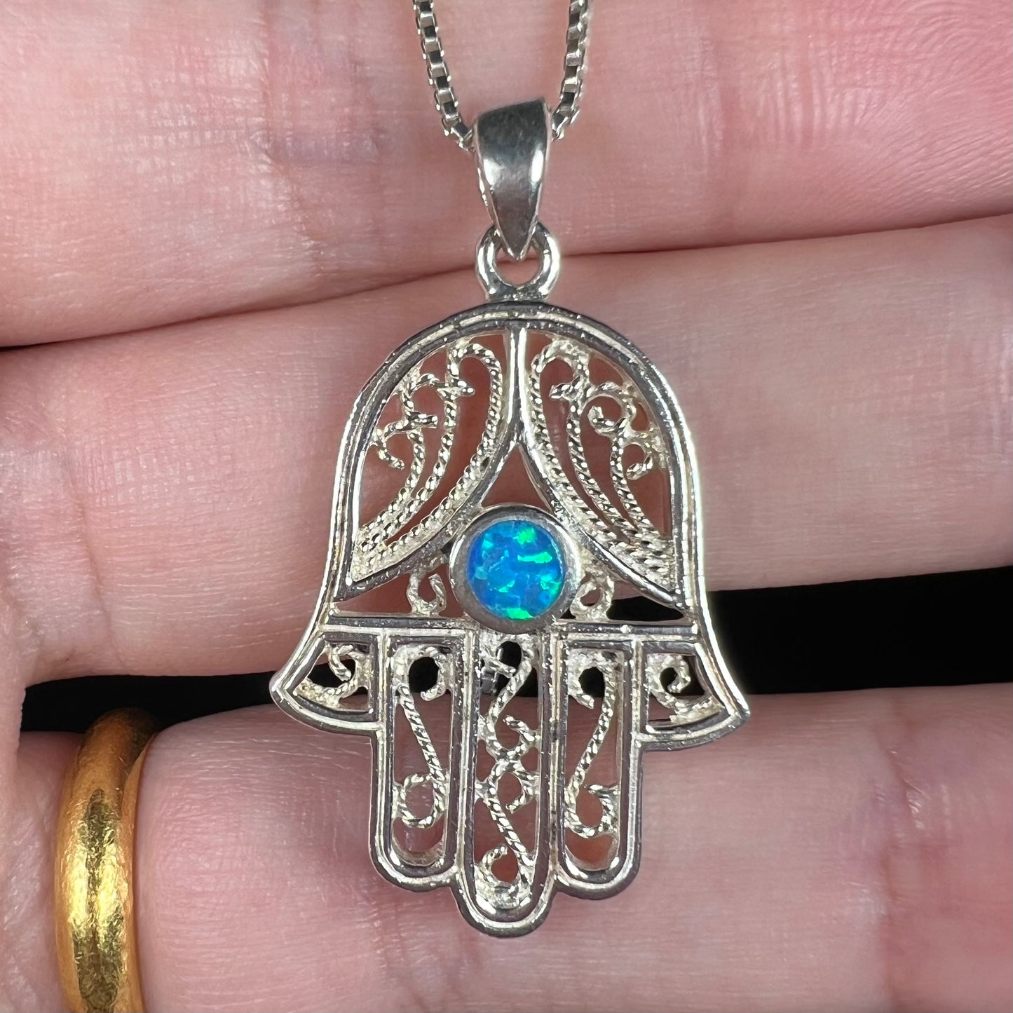 A sterling silver and filigree-accented hamsa hand necklace set with a round lab-created opal.