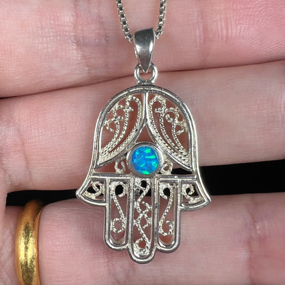 A sterling silver and filigree-accented hamsa hand necklace set with a round lab-created opal.