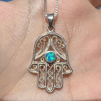 A sterling silver and filigree-accented hamsa hand necklace set with a round lab-created opal.