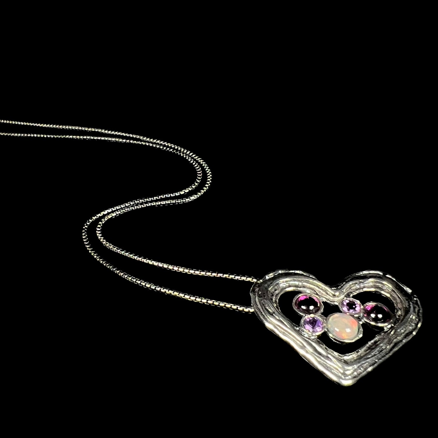 A sterling silver heart necklace set with a round Ethiopoian opal, two amethysts, and two rhodolite garnets.