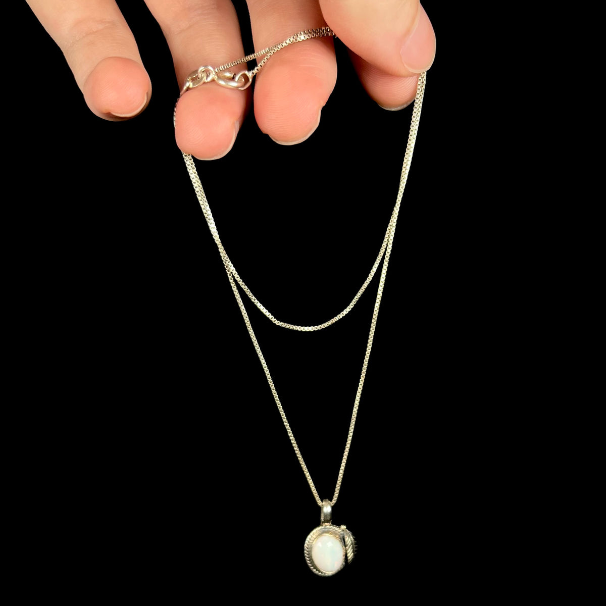 Sterling silver Southwest-style opal pendant necklace dangled from hand by its box chain