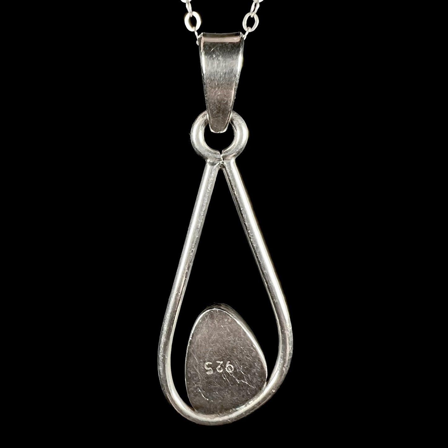 Back side of Modernist-style sterling silver opal doublet pendant, shown on chain against black backdrop.  "925" is seen on the pendant.