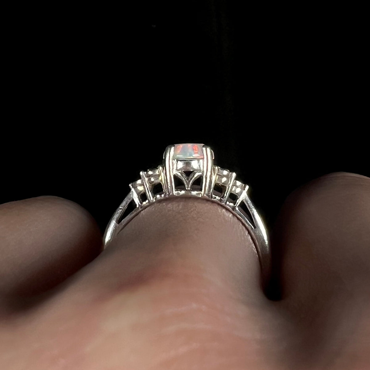 Side gallery view of a sterling silver opal ring with diamond accents in shoulders, worn on hand.