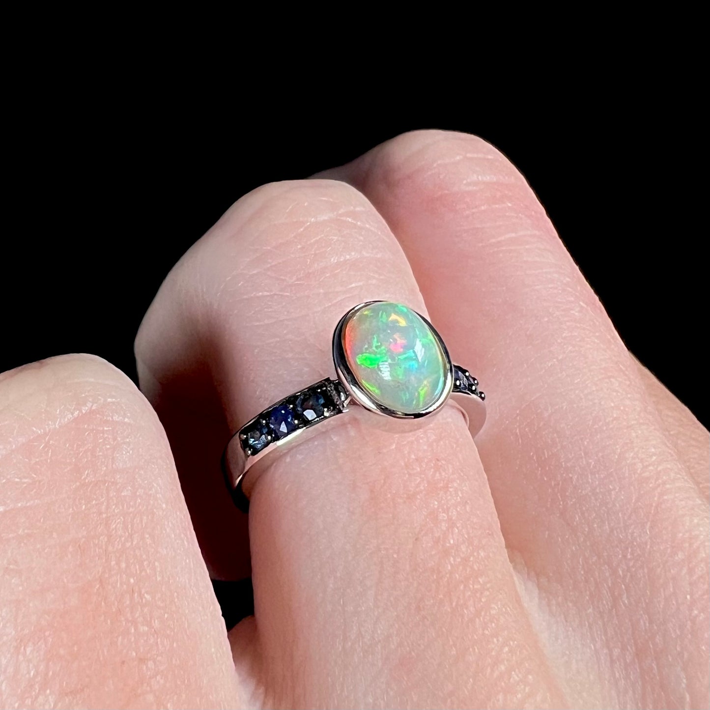A sterling silver opal ring with dark blue accent stones worn on a hand against a black background, shown at an angle.
