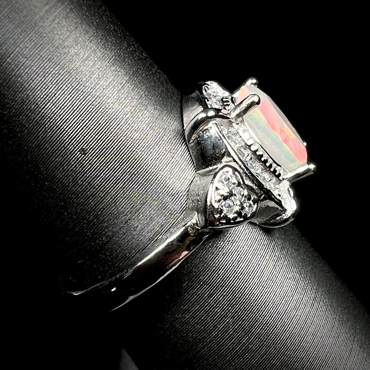 Side view of sterling silver Ethiopian opal ring on display, focused on ring's shank and CZ heart design