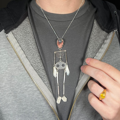 Person wearing a large sterling silver skeleton statement necklace with Mexican cantera opal skull around neck against dark shirt