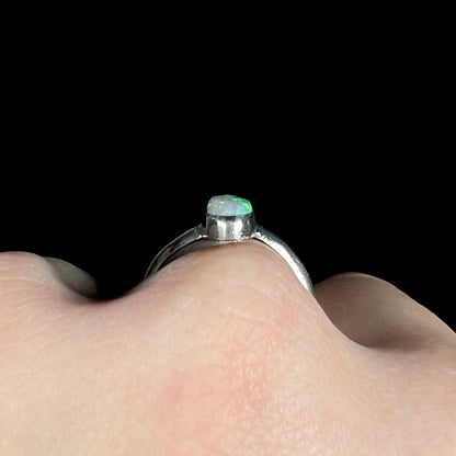 Side gallery profile view of a sterling silver opal solitaire ring worn on a hand; the top of the opal's dome is visible.