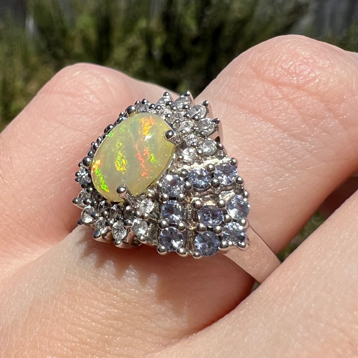 Angled close-up of sterling silver fire opal and tanzanite cluster ring, worn on finger in natural light