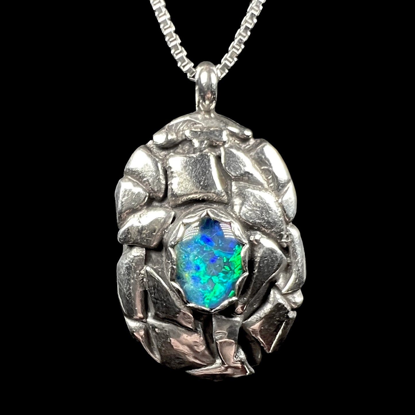 Front of a sterling silver pinecone-inspired opal triplet pendant, shown against a black background.