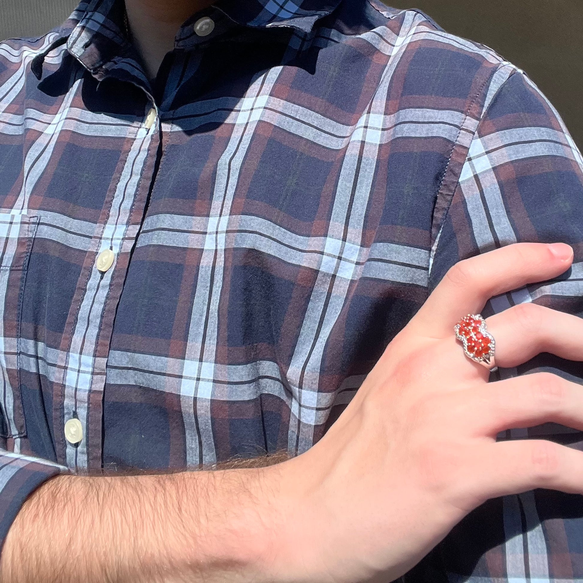 Person resting hand on their opposing shoulder in sunlight while wearing a sterling silver ring set with orange Mexican fire opals.