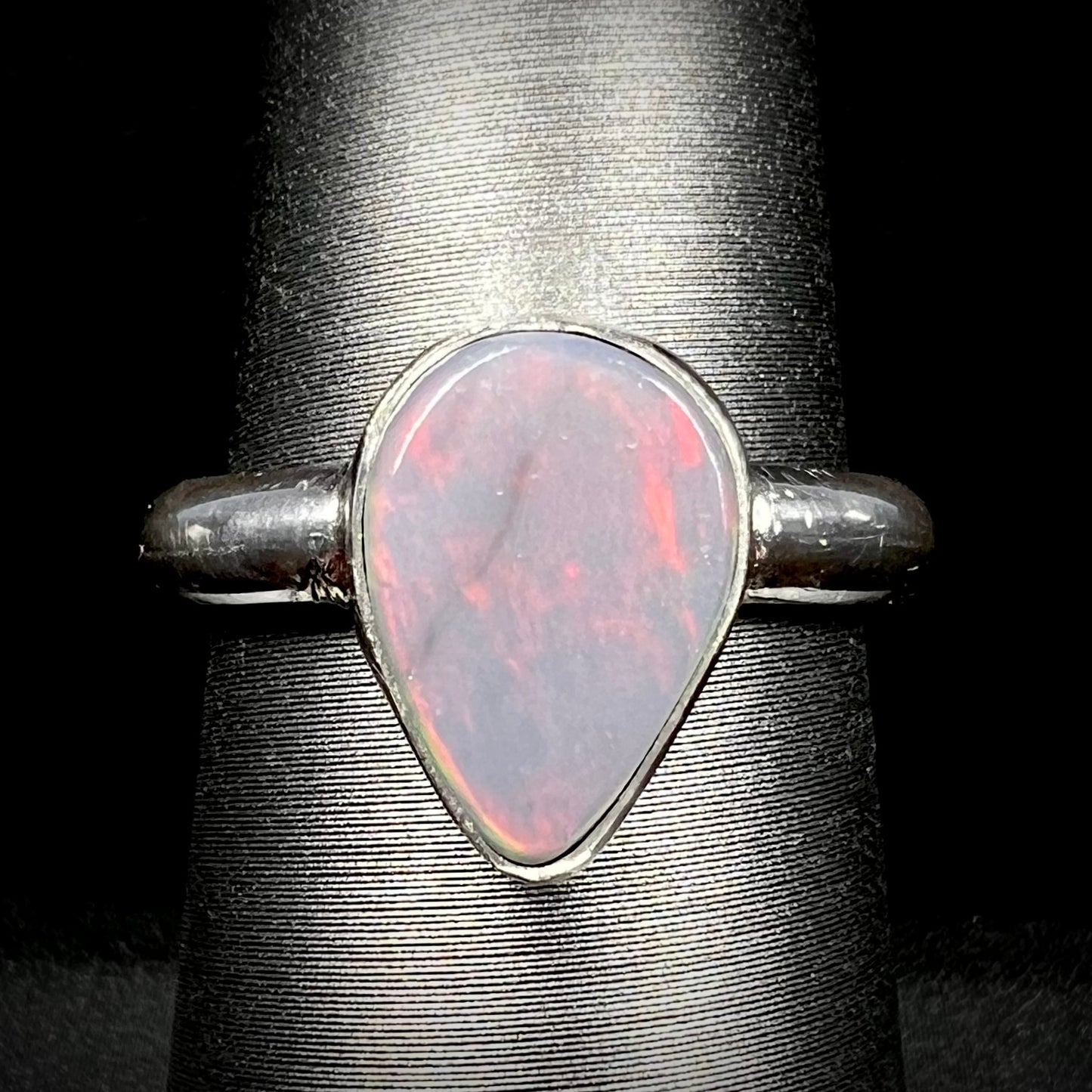 Close-up of an upsidedown pear shaped Australian dark opal solitaire ring in sterling silver with a subtle red flash of color, shown on a ring display.