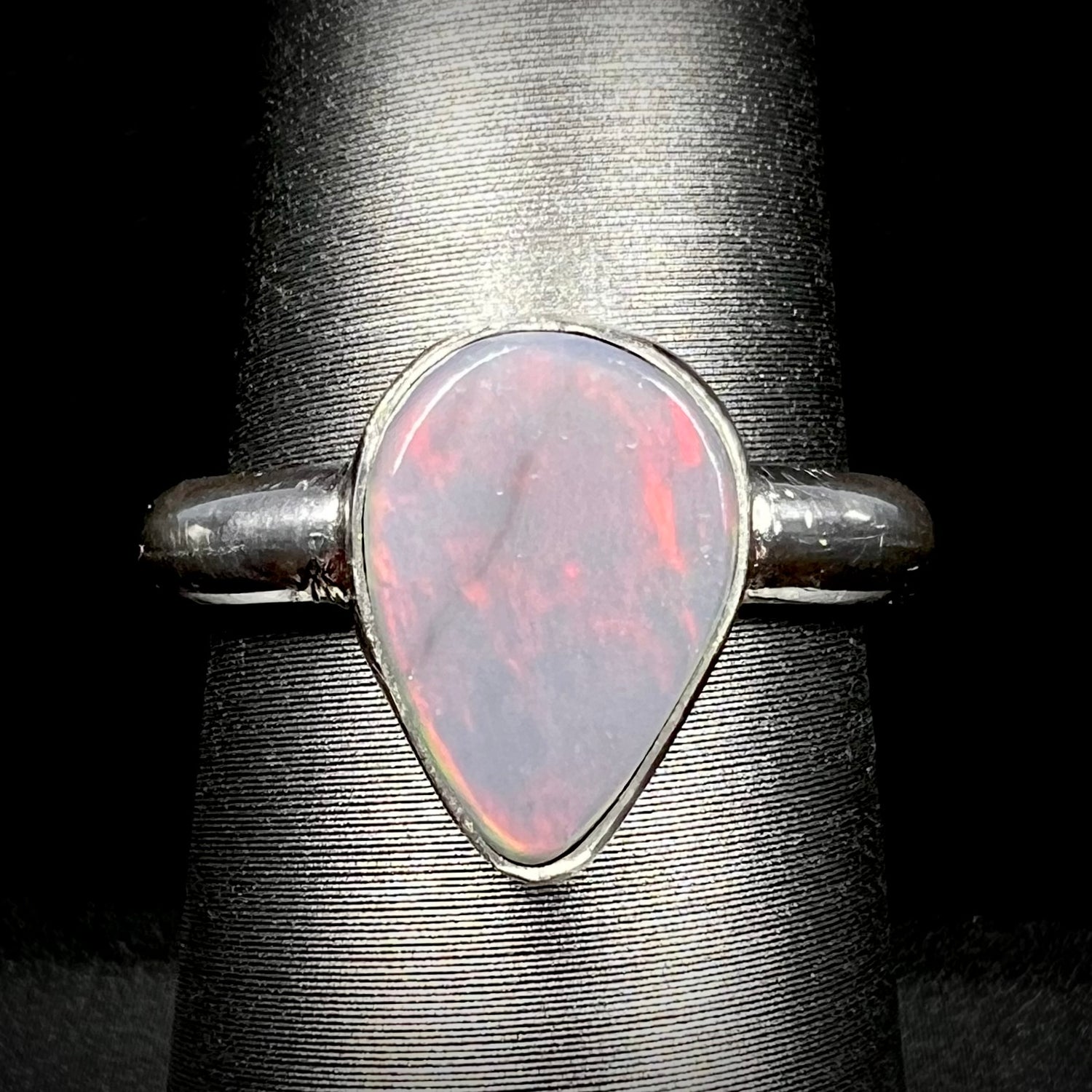 Close-up of an upsidedown pear shaped Australian dark opal solitaire ring in sterling silver with a subtle red flash of color, shown on a ring display.