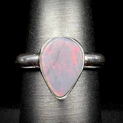 Close-up of an upsidedown pear shaped Australian dark opal solitaire ring in sterling silver with a subtle red flash of color, shown on a ring display.
