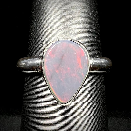 Close-up of an upsidedown pear shaped Australian dark opal solitaire ring in sterling silver with a subtle red flash of color, shown on a ring display.