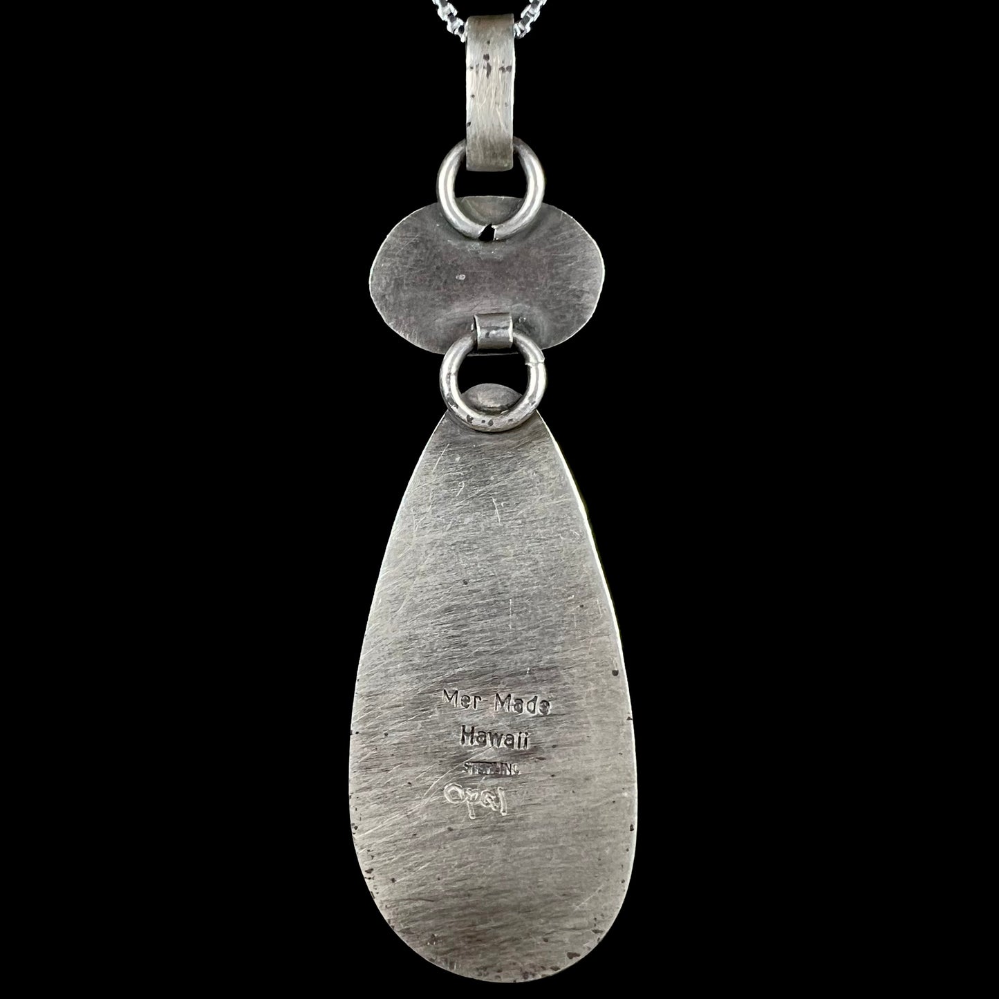 Back side of sterling silver pendant stamped "Mer Made Hawaii STERLING" and etched with the word "Opal".