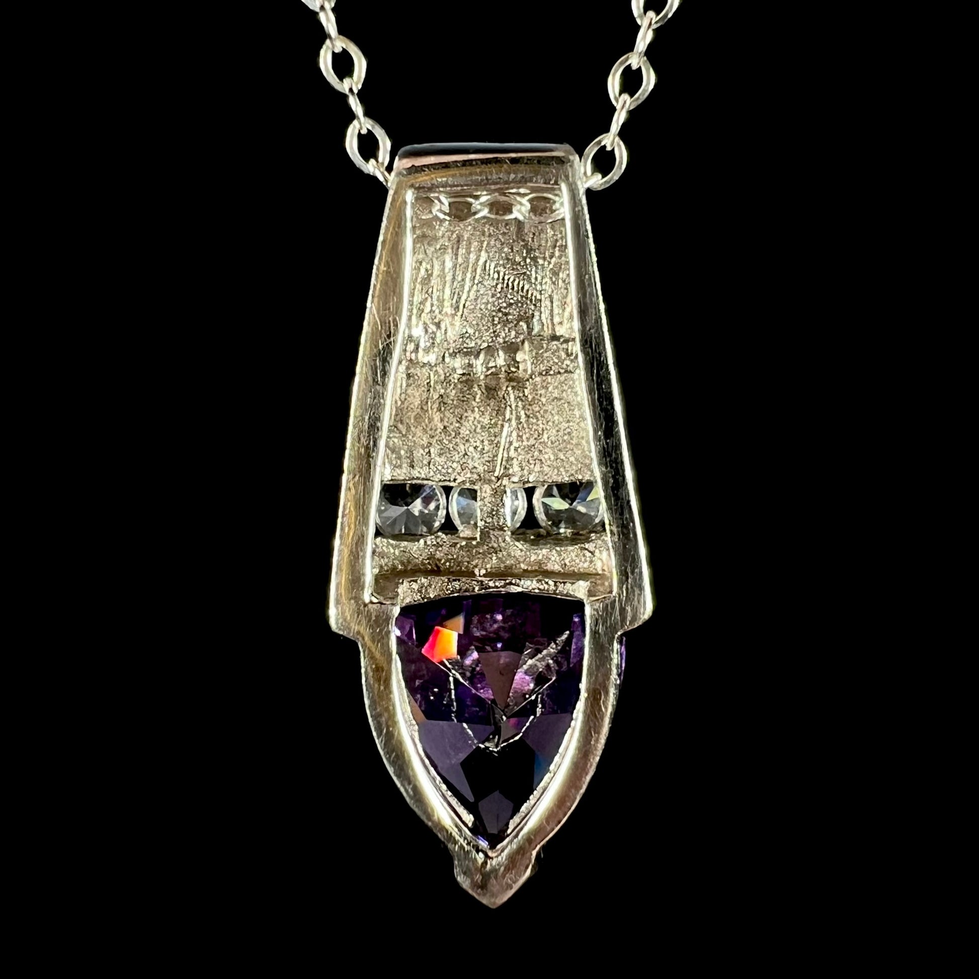 Back side of a sterling silver pendant set with colorless and purple CZ stones, shown on a silver cable chain.  A "925" hallmark stamp is visible.