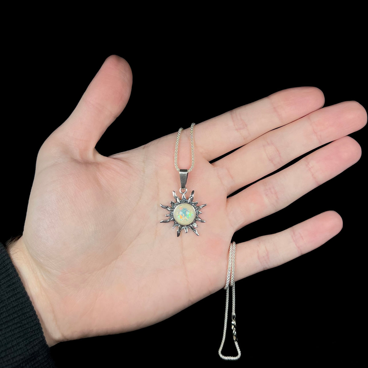 Hand holding a sterling silver sun pendant mounted with a round imitation opal under LED studio light.
