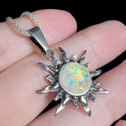 A sterling silver imitation foil-in-glass opal pendant with a solar-design motif, shown close-up from an angle resting on fingers.