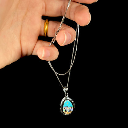 A sterling silver Southwest-style opal and turquiose inlay pendant, held by a hand from its chain.