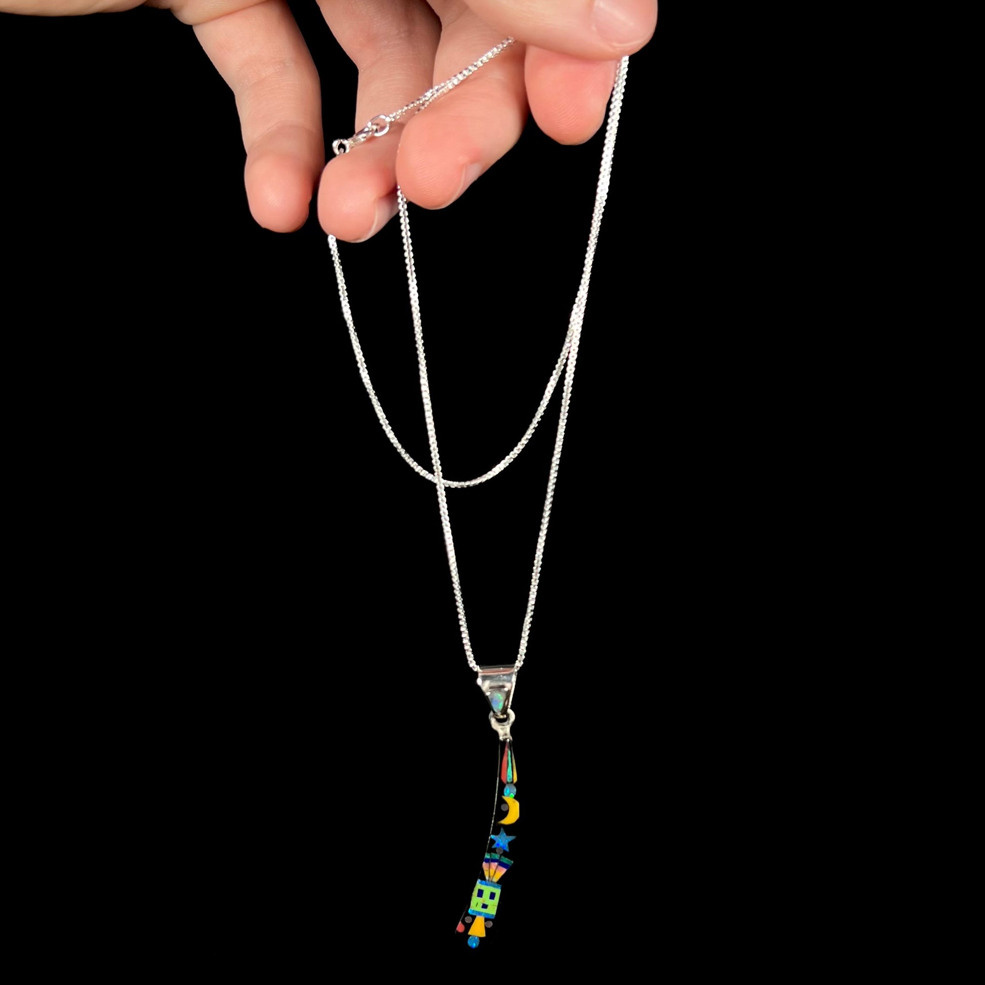 A Southwest-style sterling silver onyx and gemstone inlay necklace dangled by a hand from its chain against black background.