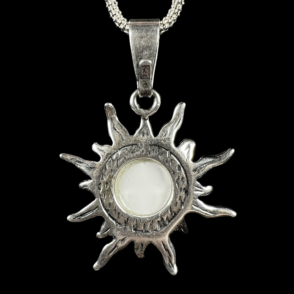 Back side of sterling silver sun design pendant featuring a clip-on bail stamped "925" in a rectangle.  The pendant's back is open showing the white backing of the mounted imitation opal.