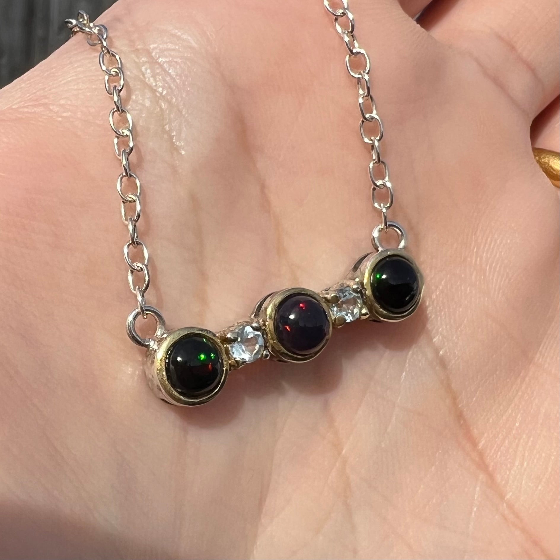 A three-stone black Ethiopian opal and white topaz necklace in two-tone sterling silver.