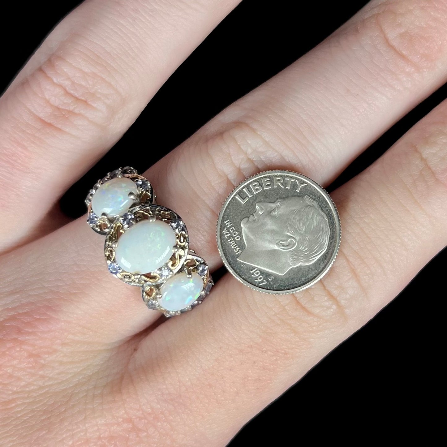 Hand wearing a sterling silver three-stone Australian opal and tanzanite women's ring next to a US dime coin for scale.