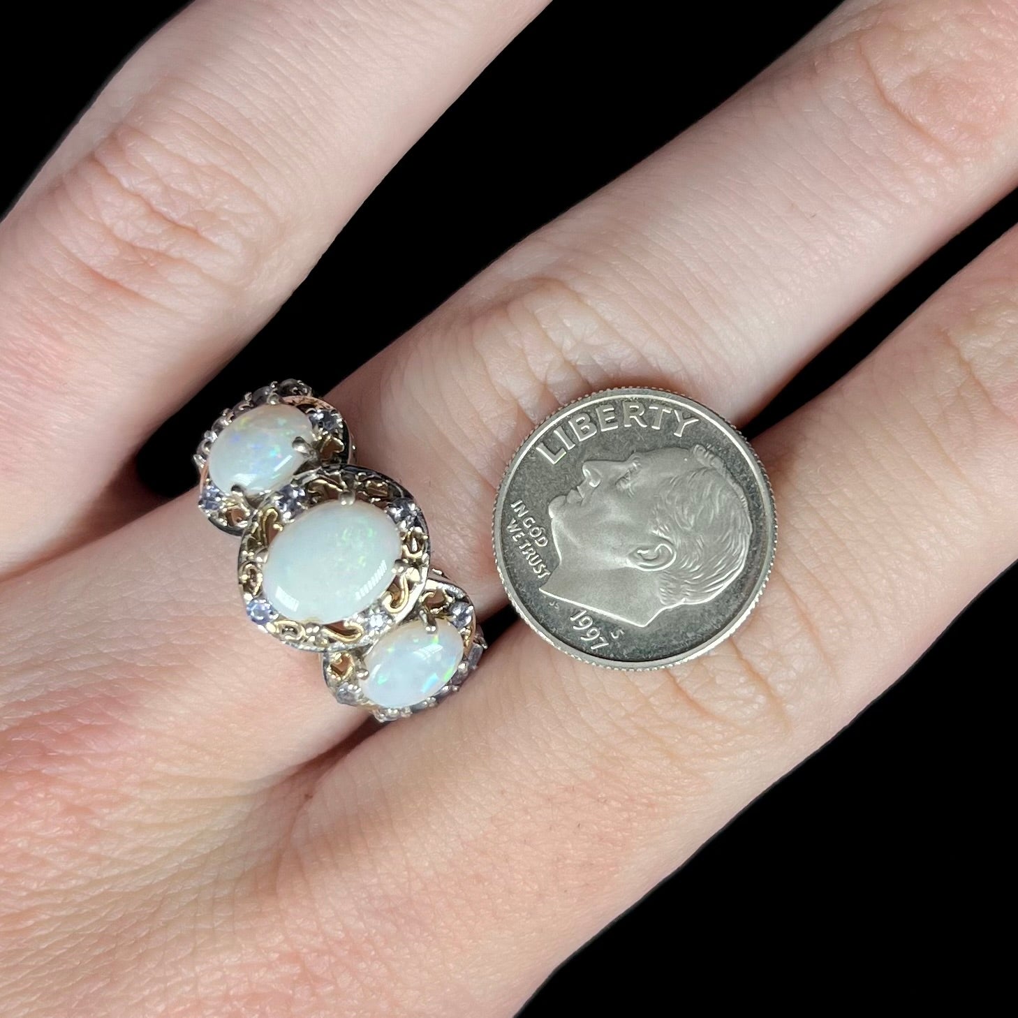 Hand wearing a sterling silver three-stone Australian opal and tanzanite women's ring next to a US dime coin for scale.