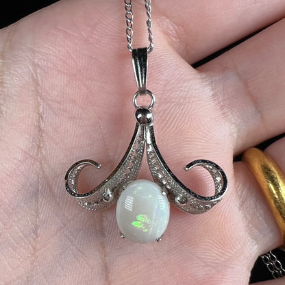 A Sorrento brand sterling silver Australian white opal pendant with a green flash shown close-up in a hand.