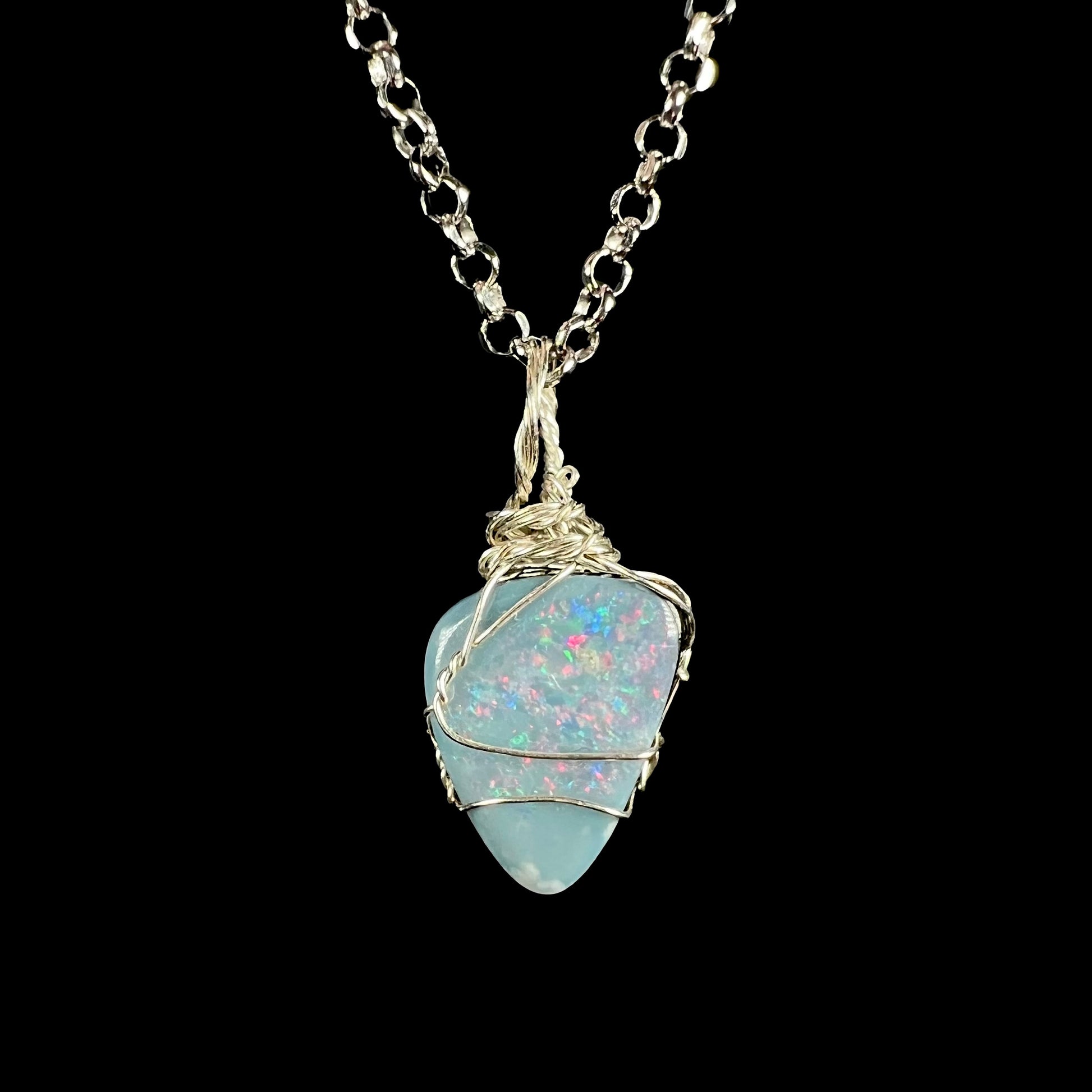 A dainty women's sterling silver wire wrapped Australian dark opal doublet pendant on a steel cable chain, shown against black background.