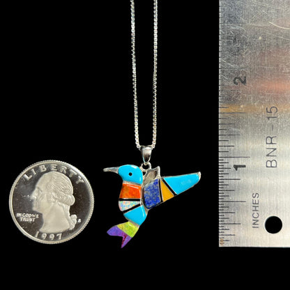 A multi-stone inlay hummingbird necklace in sterling silver, shown next to a quarter coin and ruler.